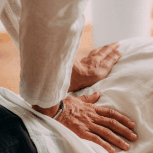 Eine Person führt eine Shiatsu-Behandlung auf einer liegenden Person durch und übt sanften Druck mit den Händen aus.