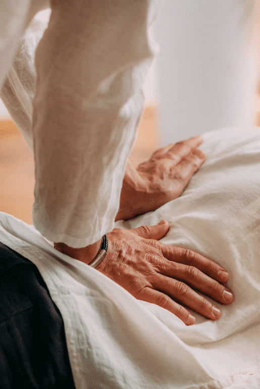 Eine Person führt eine Shiatsu-Behandlung auf einer liegenden Person durch und übt sanften Druck mit den Händen aus.