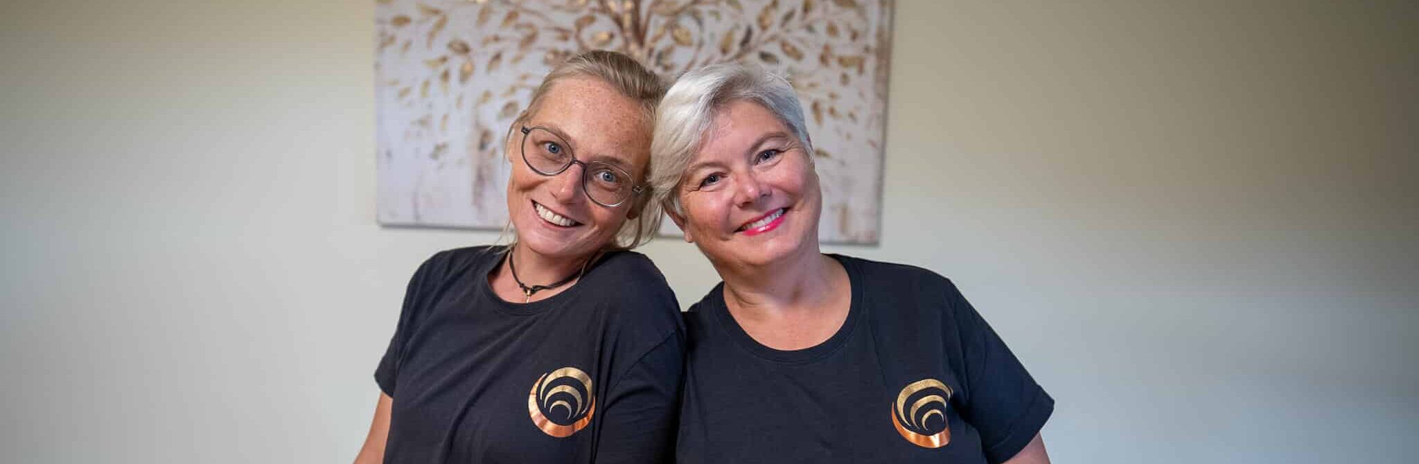 Zwei Personen in Shiatsu-Shirts lächeln in die Kamera, vor bildhaftem Hintergrund einer beruhigenden Atmosphäre.