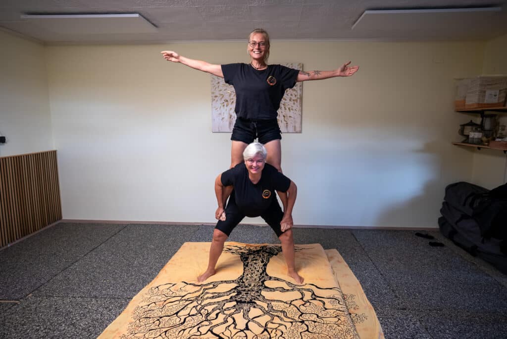 Zwei Personen üben eine Shiatsu-Balancetechnik auf einer Matte mit Baumdesign.