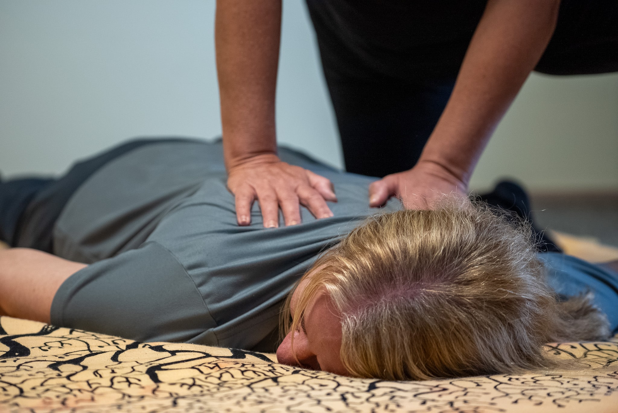 Eine Person erhält eine Shiatsu-Massage auf einer Matte, Fokus auf Hände des Therapeuten auf dem Rücken.