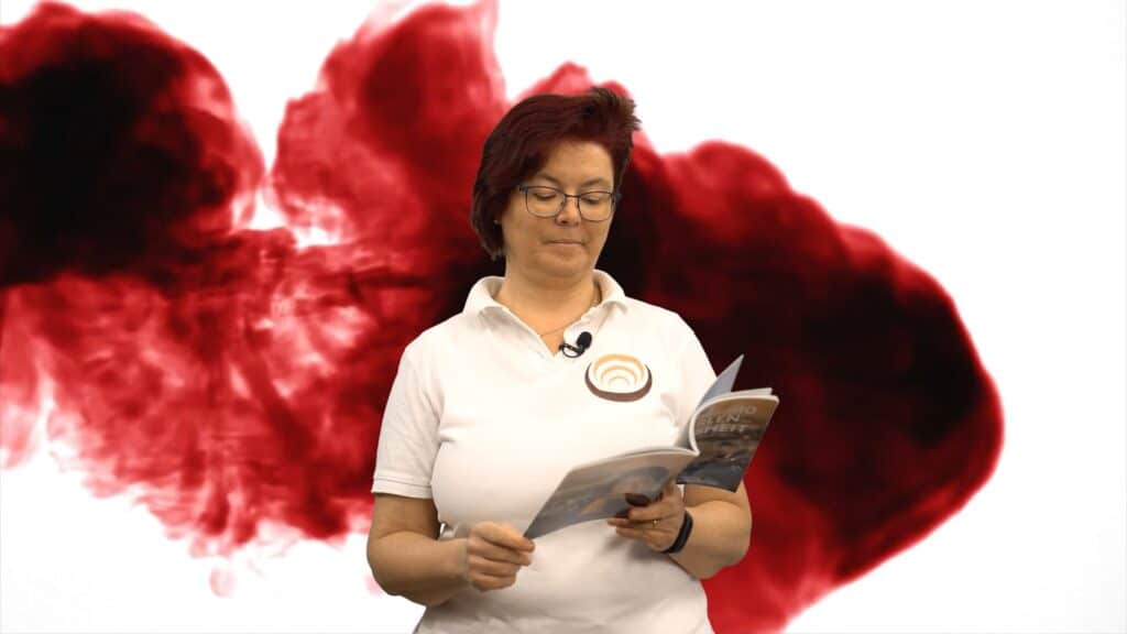 Person in weißem Polohemd mit Logo liest ein Buch vor einem rot-schwarzen Hintergrund, das Shiatsu thematisiert.